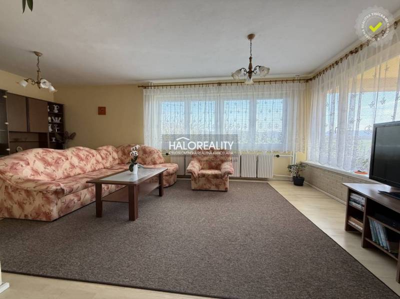 Predaj, rodinný dom Oslany - EXKLUZÍVNE HALO REALITY - Obývačka s kobercom, kvetovanou sedačkou a podlahou s dreveným dekorom v rodinnom dome.