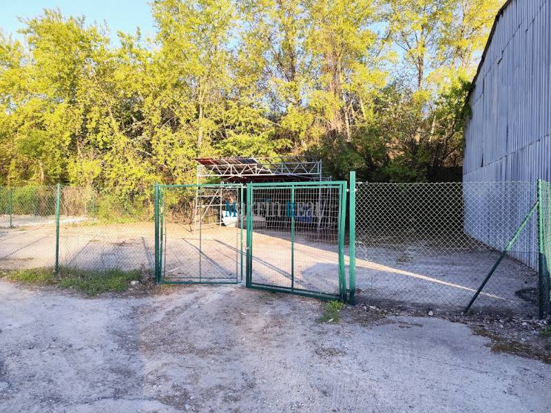 Prenájom oploteného pozemku – Nitra, Mlynárce – 390 m² - Plot s bránou a kovovou stavbou obklopený stromami v komerčnej časti Nitry.