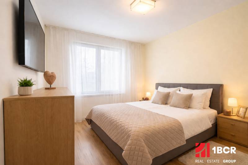 EXKLUZÍVNY 3-IZBOVÝ BYT V SÚKROMNOM KOMPLEXE |2x PARKING | NA PIESKU,  - Spálňa v 3-izbovom byte so sivou posteľou, podlahou s dreveným dekorom a TV na stene.