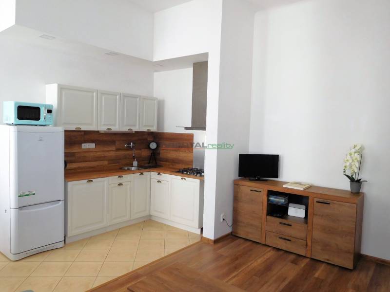 Predaj - štýlový 1,5i byt  v srdci Starého Mesta - Marianska, BA - Kuchynka v 2-izbovom byte, svetlý interiér, podlaha s dreveným dekorom, biela chladnička.