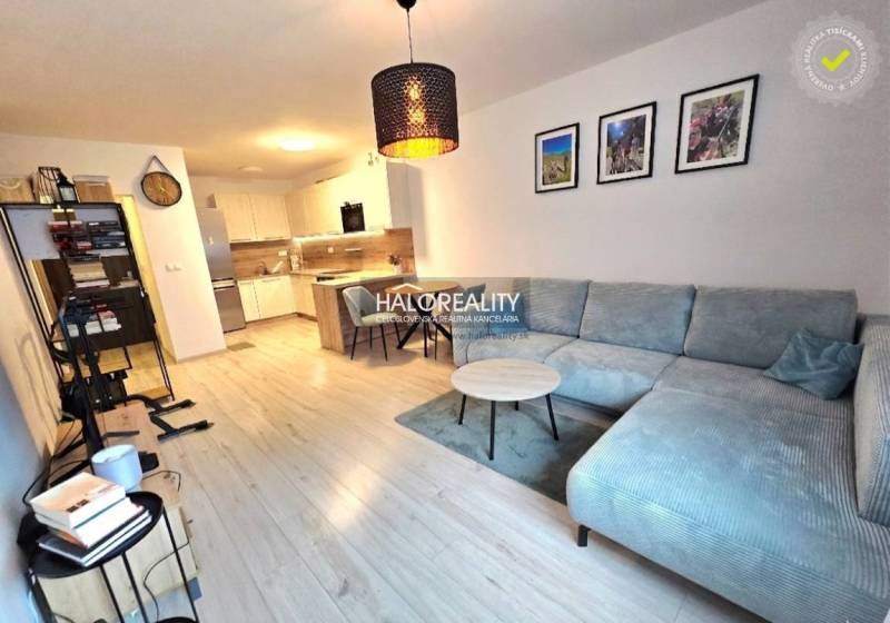 Predaj, dvojizbový byt Bratislava Podunajské Biskupi... - Obývačka s rohovou sedačkou, kuchyňou a podlahou s dreveným dekorom v 2-izbovom byte.