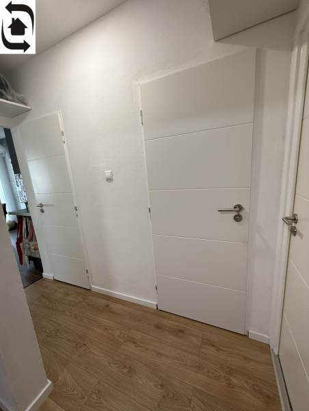 4 Izbový byt na Kríkovej ulici na predaj - Chodba v 4-izbovom byte s bielymi dverami a podlahou s dreveným dekorom.