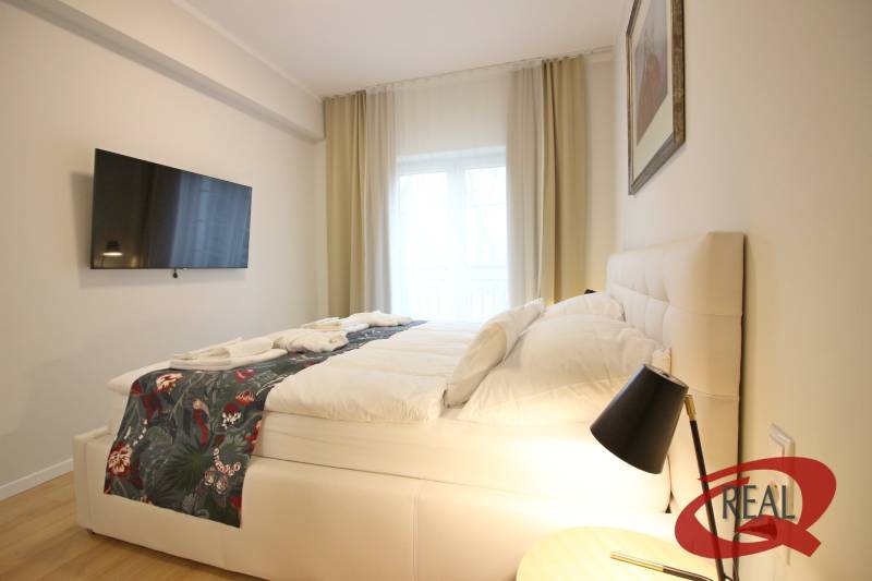 **SKVELÁ INVESTÍCIA**REZIDENCIA OPERA**KÚPELE TURČIANSKE TEPLICE** - Svetlá spálňa v 2-izbovom byte s TV, veľkou posteľou a nočným stolíkom.