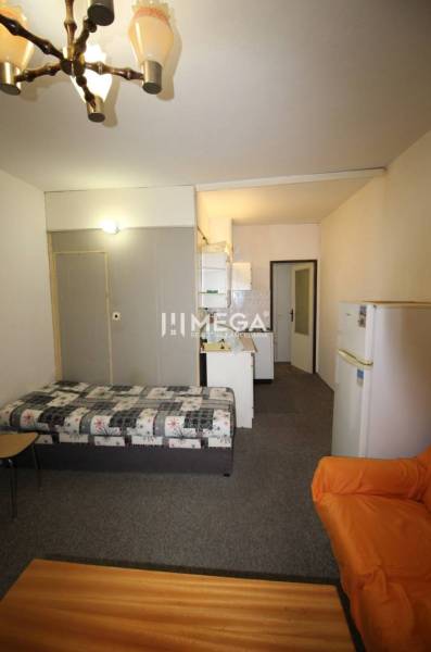 NA PRENÁJOM - Garsónka v pôvodnom stave na Sídlisku III v meste Humenn - Rekreačný apartmán s posteľou, kuchynským kútom a pohovkou, osvetlený lustrom.