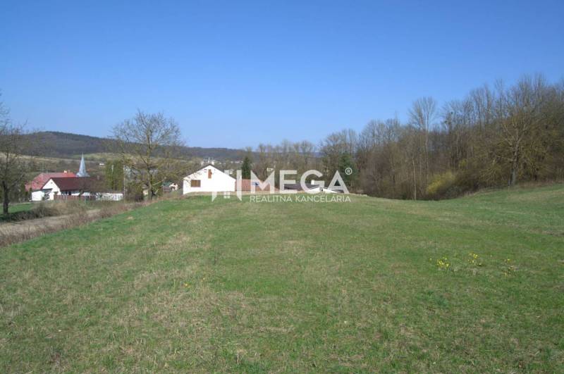 ZNÍŽENIE CENY-PREDAJ VEĽKÉHO POZEMKU (7.048 m2) v  obci Tovarnianska P - Pozemky - bývanie v Tovarnianskej Polianke, s výhľadom na domy a stromy pod modrou oblohou.