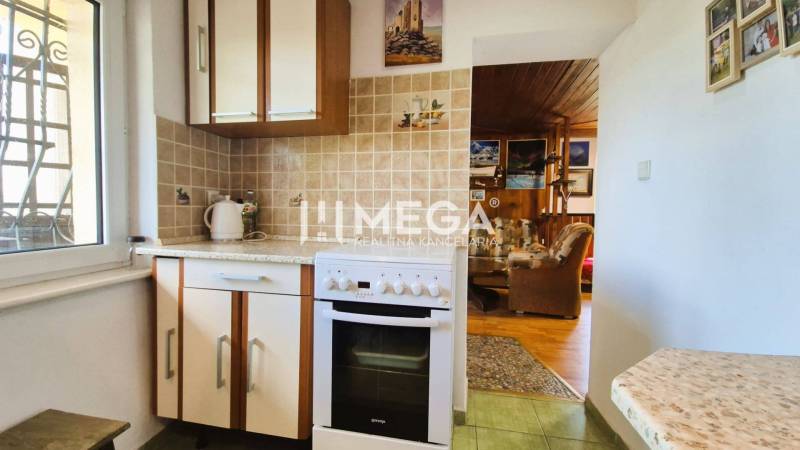 PREDAJ REKREAČNEJ CHATY NA DOMAŠI časť DOBRÁ - Kuchynka v chate so sporákom, keramickým obkladom a prechodom do obývačky s dreveným dekorom.