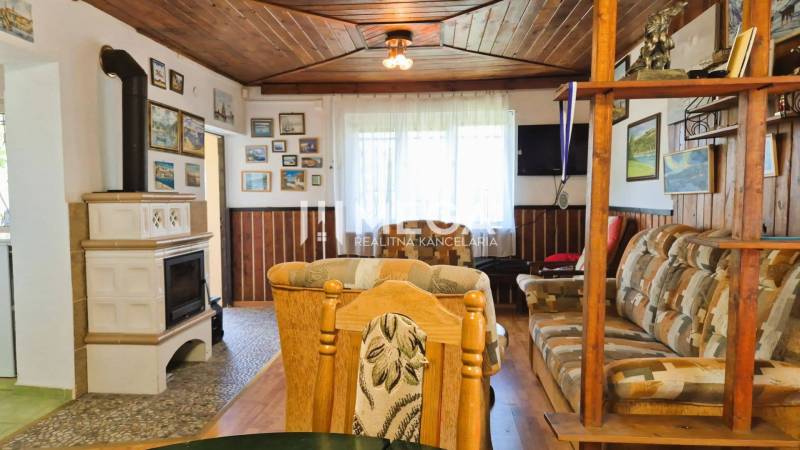 PREDAJ REKREAČNEJ CHATY NA DOMAŠI časť DOBRÁ - Interiér chaty so sedacou súpravou, kachľovou pecou a podlahou s dreveným dekorom.