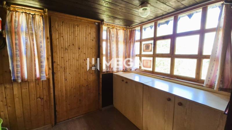 PREDAJ REKREAČNEJ CHATY NA DOMAŠI časť DOBRÁ - Interiér chaty s dreveným obkladom, veľkými oknami a farebnými závesmi.