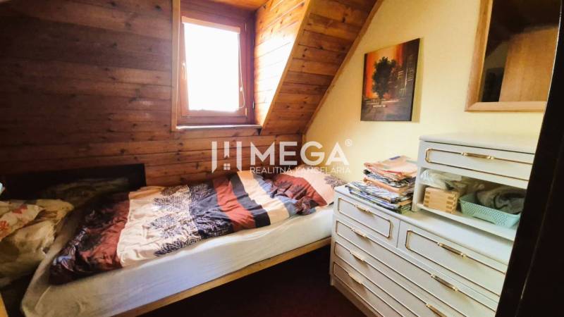 PREDAJ REKREAČNEJ CHATY NA DOMAŠI časť DOBRÁ - Izba v chate s posteľou, drevenými stenami a komodou.