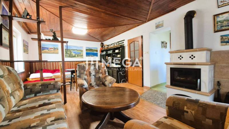 PREDAJ REKREAČNEJ CHATY NA DOMAŠI časť DOBRÁ - Chata s krbom a podlahou s dreveným dekorom, sedačkou a dekoratívnymi obrazmi.