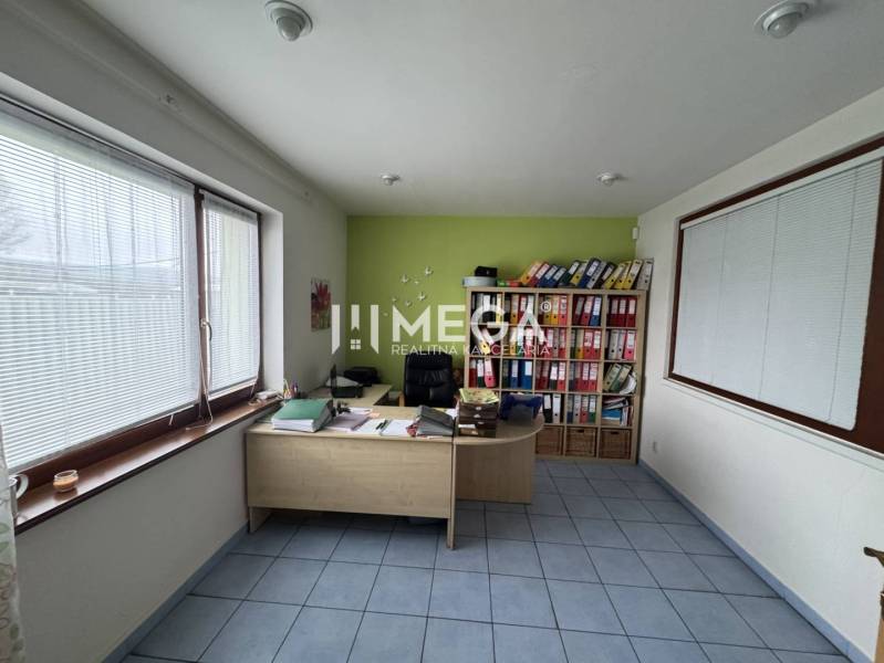 NA PREDAJ: OBJEKT VHODNÝ NA PODNIKANIE-SKLADOVANIE A SLUŽBY - Kancelária s pracovným stolom, poličkami na šanóny a veľkými oknami s roletami.