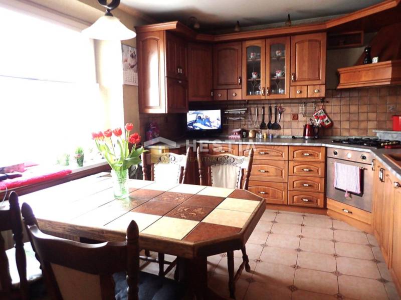 ZNÍŽENÁ CENA Veľký 2-izbový investičný byt Senica - 73,54 m² - Kuchyňa s dreveným dekorom, jedálenským stolom a kvetmi v 2-izbovom byte.