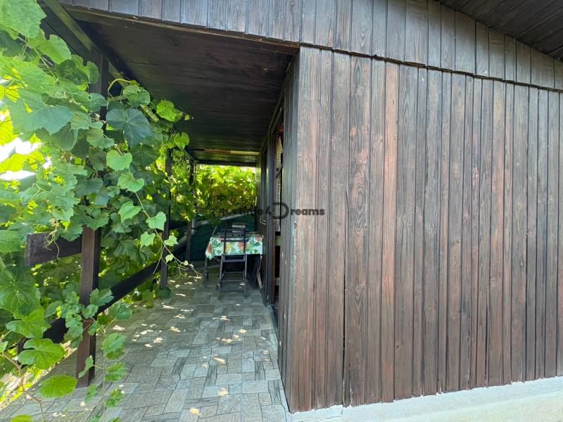 Na predaj: Ovocná záhrada v Leviciach - Drevená veranda so stolom a stoličkami, obklopená zeleňou v Záhradách blízko Levíc.