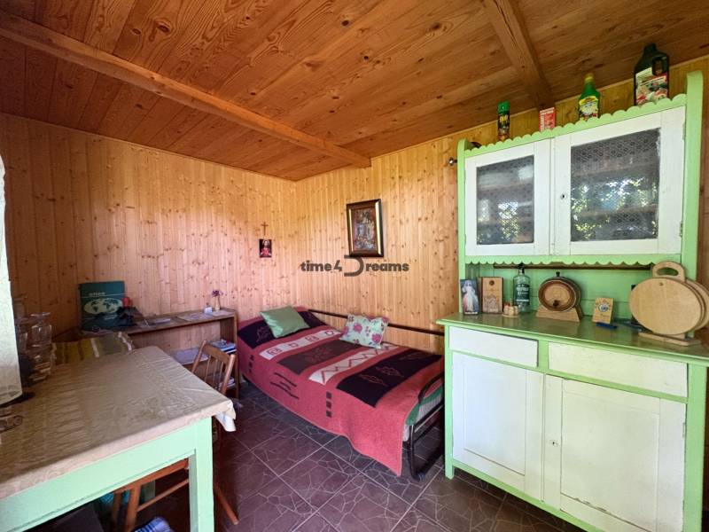 Na predaj: Ovocná záhrada v Leviciach - Drevený interiér záhrady s jedálenským stolom, pohovkou, skrinkou a dekoráciami.