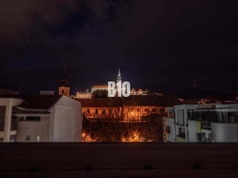 PRIESTRANNÝ Apartmán v CENTRE s výnimočným výhľadom - Nočná scéna Nitry s výhľadom na osvetlený hrad a okolité budovy.