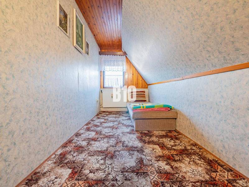 POD HRADOM bývanie alebo podnikanie - Podkrovná izba v rodinnom dome s tapetami a farebným kobercom na podlahe.