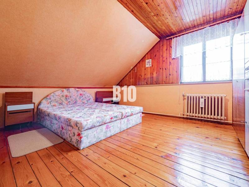 POD HRADOM bývanie alebo podnikanie - Podkrovná izba s dvojlôžkovou posteľou, dreveným stropom a podlahou s dreveným dekorom.