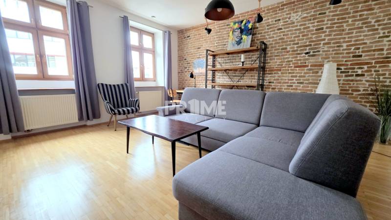 JEDINEČNÝ 2i byt, REKONŠT., 2 X .SAMOST.IZBA, Hviezdoslavovo nám.  - Obývačka vo svetlých tónoch s pohovkou a tehlovou stenou v 2-izbovom byte.