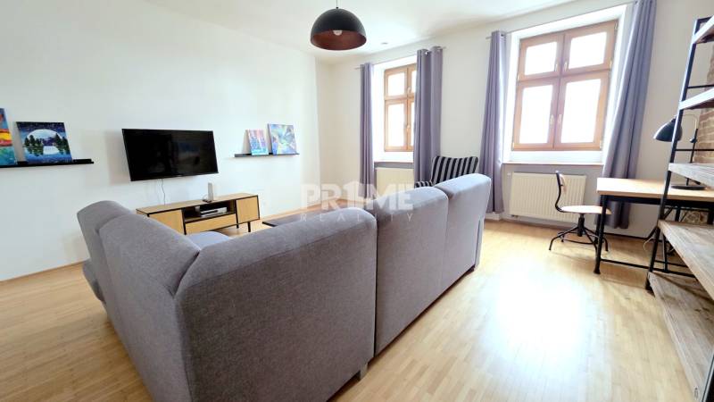 JEDINEČNÝ 2i byt, REKONŠT., 2 X .SAMOST.IZBA, Hviezdoslavovo nám.  - Obývacia izba v 2-izbovom byte so sivou sedačkou a podlahou s dreveným dekorom.