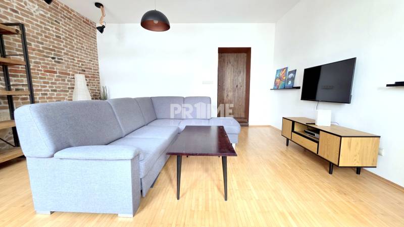 JEDINEČNÝ 2i byt, REKONŠT., 2 X .SAMOST.IZBA, Hviezdoslavovo nám.  - Obývacia izba s pohovkou, tehlovou stenou a podlahou s dreveným dekorom v 2-izbovom byte.