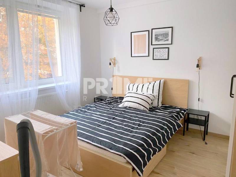 ŠTÝLOVÝ 2i byt, NOVOSTAVBA, BALKÓN, PARKIN, Paričková ulica, NIVY - Izba obsahuje posteľ s pruhovaným obliečkom, biely záves, dekorácie na stene.