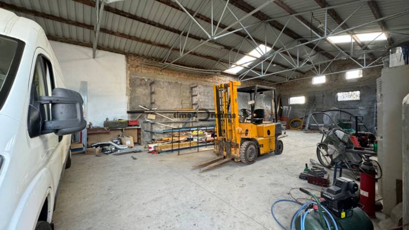 NA PREDAJ rodinný dom/polyfunkcia Komjatice  - Interiér garáže s vysokozdvižným vozíkom a dodávkou, obklopený rôznym náradím a materiálom.