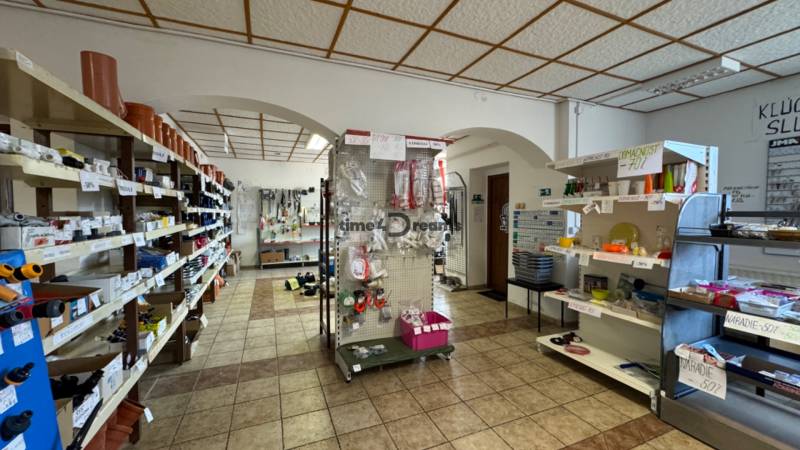 NA PREDAJ rodinný dom/polyfunkcia Komjatice  - Interiér železiarstva s regálmi plnými potrubí, nástrojov a domácich produktov.