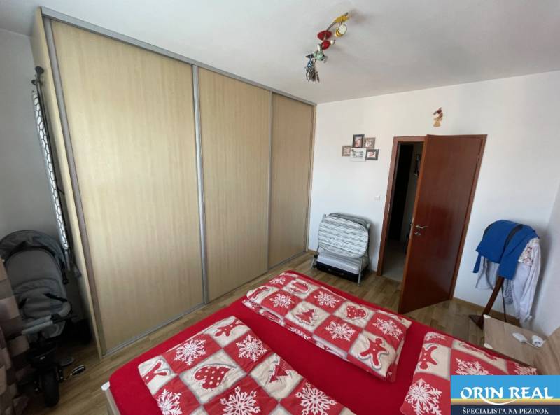 PREDAJ PRIESTRANNÉHO 3 IZB. BYTU NA MUŠKÁTE S GARÁŽOVÝM STÁTIM - Spálňa s podlahou s dreveným dekorom, vstavanou skriňou a červenou posteľnou bielizňou.