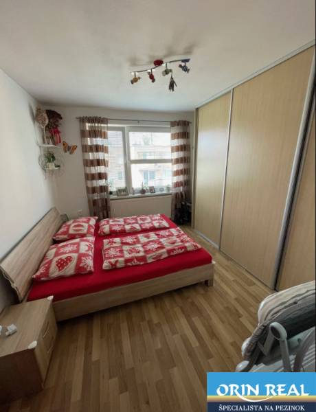 PREDAJ PRIESTRANNÉHO 3 IZB. BYTU NA MUŠKÁTE S GARÁŽOVÝM STÁTIM - Spálňa v 3-izbovom byte s posteľou, skriňou a podlahou s dreveným dekorom.