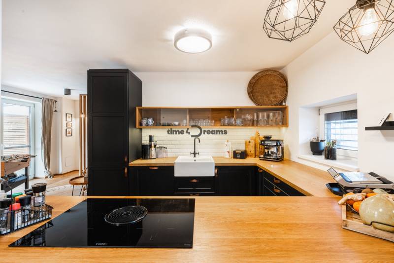 NA PREDAJ Krásny domček v Ivánke pri Nitre - Kuchyňa rodinného domu s dreveným dekorom a čiernymi skrinkami, otvorený priestor.