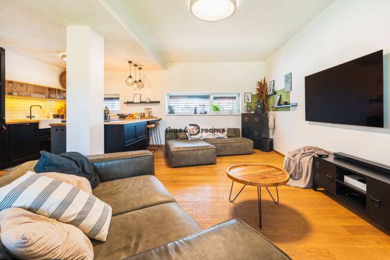 NA PREDAJ Krásny domček v Ivánke pri Nitre - Obývačka v rodinnom dome s kuchynským kútom a podlahou s dreveným dekorom.