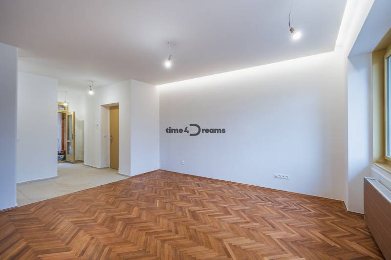 NA PREDAJ štýlový byt v centre Nitry  - Priestranná miestnosť s podlahou s dreveným dekorom v 3-izbovom byte, biele steny a okno.