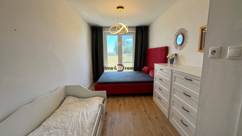 NA PREDAJ Radový rodinný dom v obci Malý Lapáš - Spálňa v rodinnom dome s posteľou, sedačkou, komodami a podlahou s dreveným dekorom.