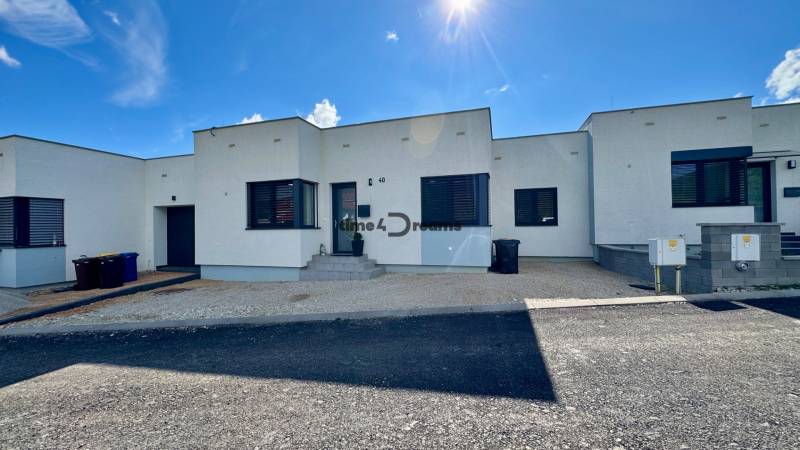 NA PREDAJ 4 izbový rodinný dom Štitáre NITRA - Rodinný dom v Štitároch s bielou fasádou a čiernymi okennými roletami, modrá obloha.