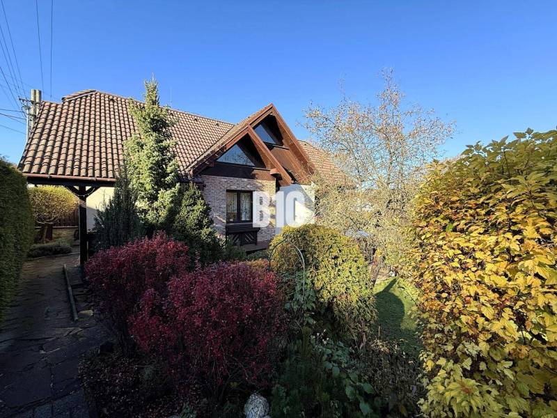 Zaujímavý rodinný dom s veľkým pozemkom, krásnou záhradou a bohatým pr - Rodinný dom v Lietave s upravenou záhradou, hnedou strechou a bohatou výsadbou.