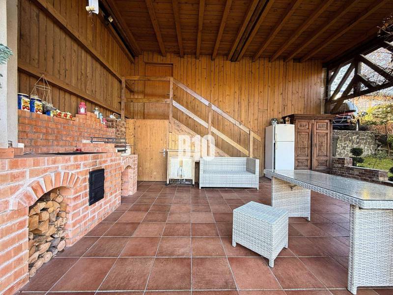 Zaujímavý rodinný dom s veľkým pozemkom, krásnou záhradou a bohatým pr - Exteriér rodinného domu v Lietave s tehlovým grilom a terasovým posedením.