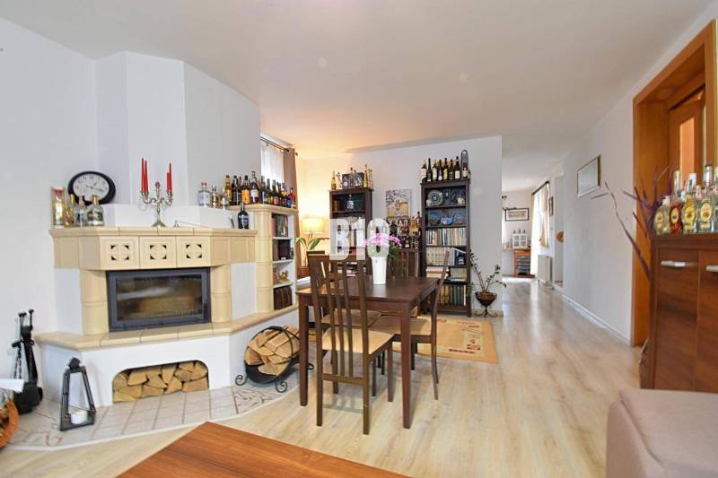 Zaujímavý rodinný dom s veľkým pozemkom, krásnou záhradou a bohatým pr - Interiér rodinného domu s krbom, jedálenským stolom a podlahou s dreveným dekorom.