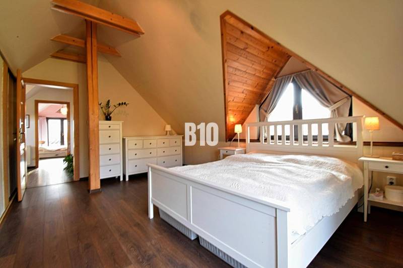 Zaujímavý rodinný dom s veľkým pozemkom, krásnou záhradou a bohatým pr - Podkrovná spálňa v rodinnom dome s dreveným dekorom a bielym nábytkom.