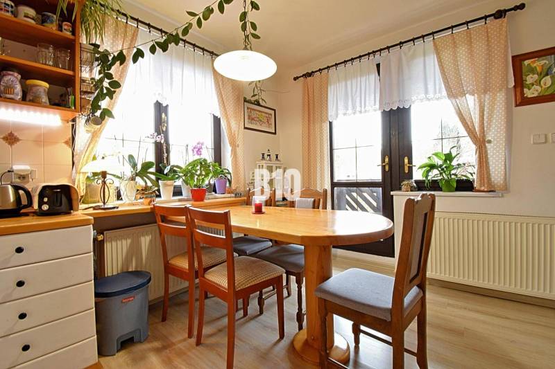 Zaujímavý rodinný dom s veľkým pozemkom, krásnou záhradou a bohatým pr - Interiér rodinného domu so stolom a stoličkami, obklopený izbovými rastlinami.