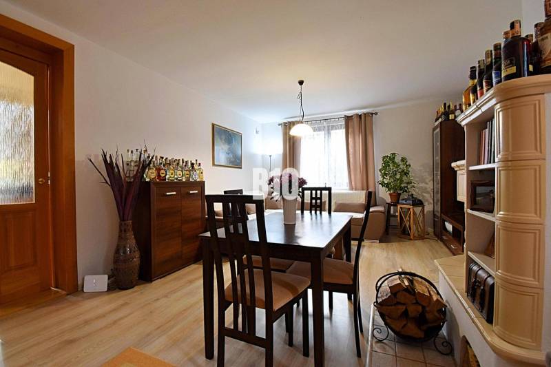 Zaujímavý rodinný dom s veľkým pozemkom, krásnou záhradou a bohatým pr - Interiér rodinného domu s podlahou s dreveným dekorom, jedálenským stolom a krbovými kachľami.