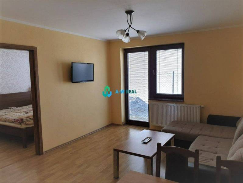 Apartmánový dom na predaj blízko termálneho kúpaliska - Obývacia izba s pohovkou, televízorom na stene a dreveným nábytkom, na ulici neuvedené.