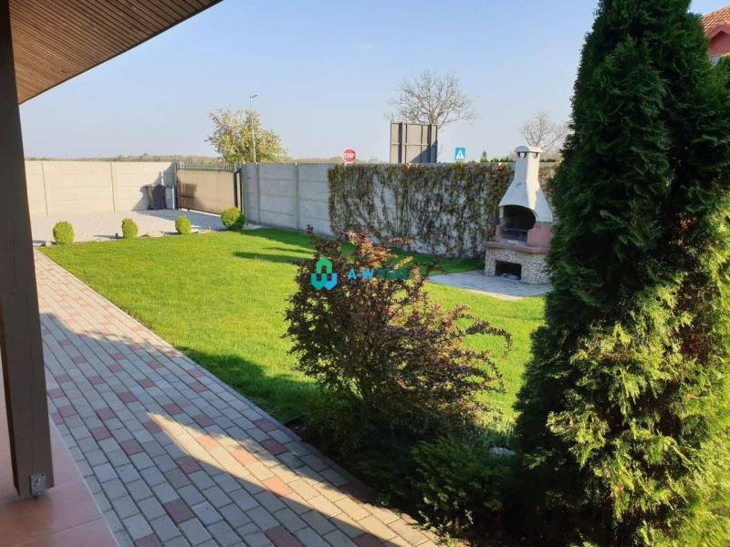 Apartmánový dom na predaj blízko termálneho kúpaliska - Na ulici neuvedené: záhrada s trávnikom, krb, obchodné priestory v pozadí.