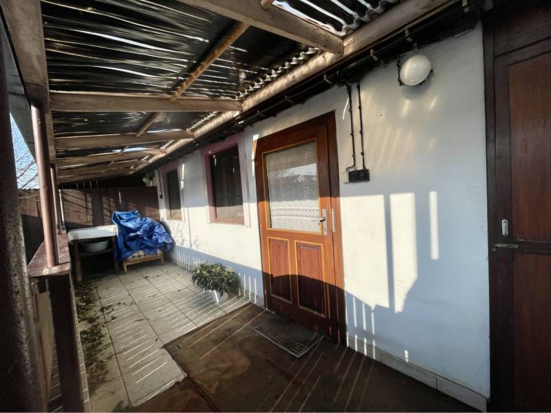 VRAKÚŇ – STARÝ RODINNÝ DOM NA PREDAJ S VEĽKÝM POZEMKOM - 24 ÁROV - Rodinný dom vo Vrakúni s terasou, rastlinou a prestrešením, na dlaždenej podlahe.