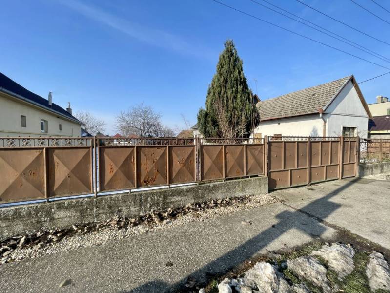 VRAKÚŇ – STARÝ RODINNÝ DOM NA PREDAJ S VEĽKÝM POZEMKOM - 24 ÁROV - Rodinný dom vo Vrakúni s kovovým plotom na neuvedenej ulici, vedľa stromu.