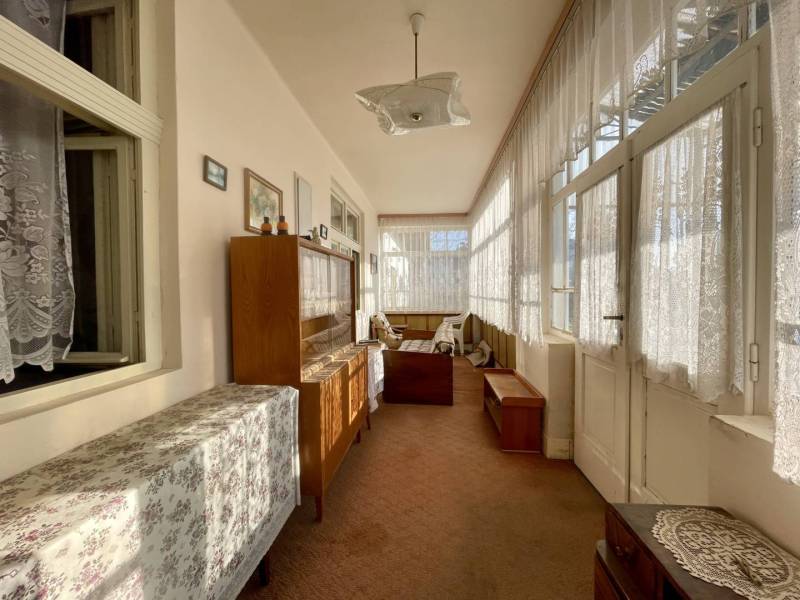 VRAKÚŇ –VEĽKÝ STAVEBNÝ POZEMOK (24 ÁROV) SO STARÝM RODINNÝM DOMOM NA P - Sklenená veranda s čipkovými závesmi a dreveným nábytkom v rodinnom dome.