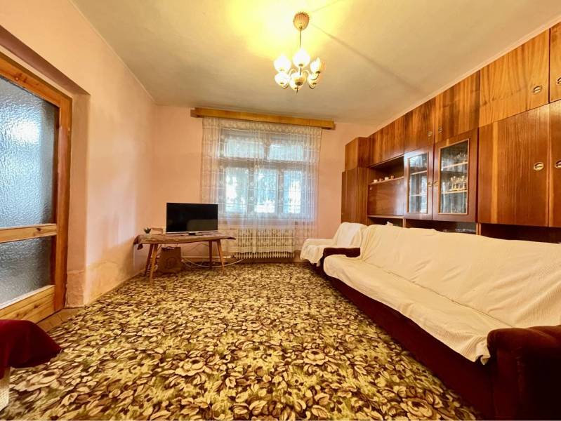 TOPOĽNÍKY – 4-IZBOVÝ RODINNÝ DOM NA PREDAJ NA 14 ÁROVOM POZEMKU - Obývacia izba v rodinnom dome s kobercom kvetinového vzoru a drevenou obývacou stenou.