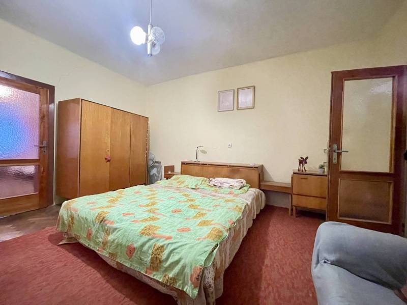 TOPOĽNÍKY – 4-IZBOVÝ RODINNÝ DOM NA PREDAJ NA 14 ÁROVOM POZEMKU - Spálňa v rodinnom dome s posteľou, skriňou, stolíkom a červeným kobercom.