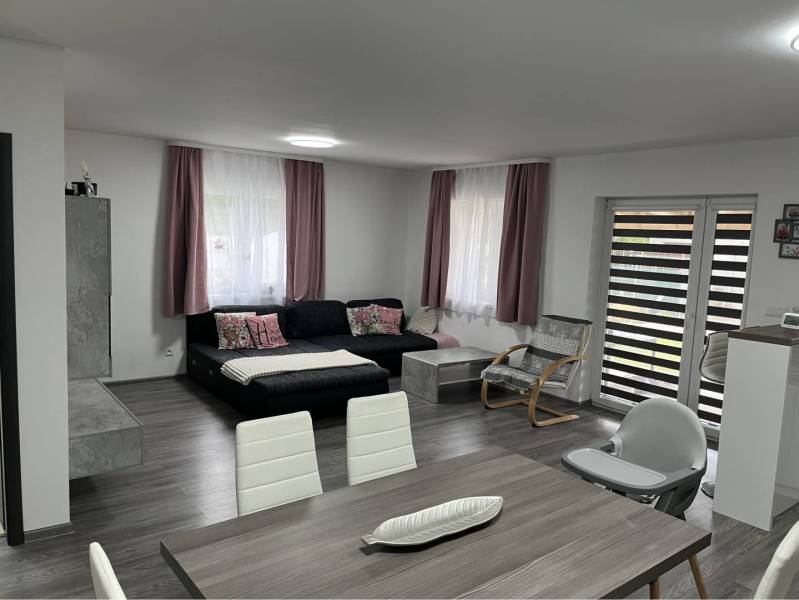 HORNÁ POTOŇ – 4-IZBOVÝ RODINNÝ DOM - NOVOSTAVBA - Interiér Rodinného domu s podlahou s dreveným dekorom, sedačkou, hojdacím kreslom a stolom.