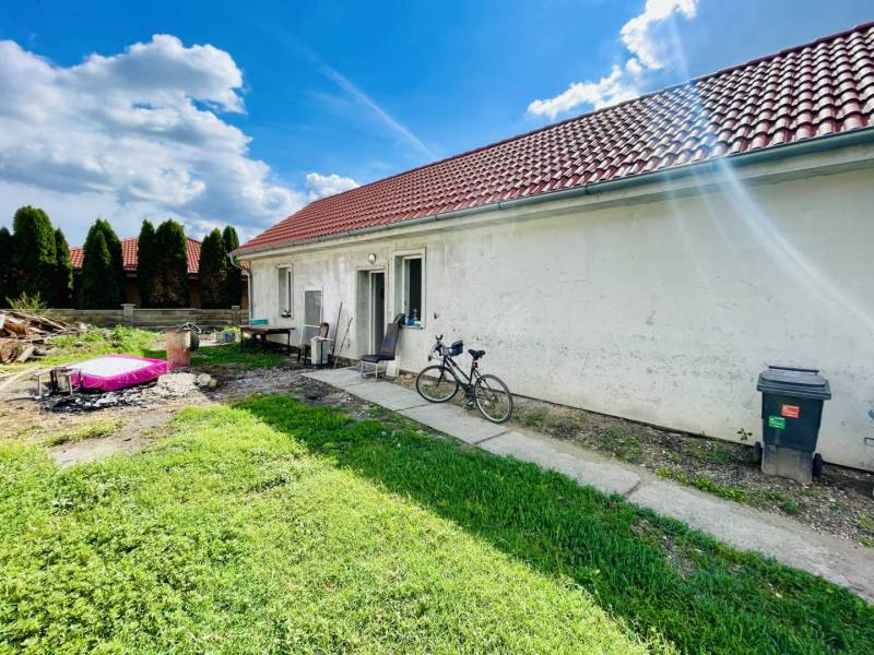 RODINNÝ DOM S ÚTULNÝM POZEMKOM NA PREDAJ V OBCI PATAŠ - Rodinný dom v Pataši s červenou strechou, bicyklom a trávnikom v záhrade.
