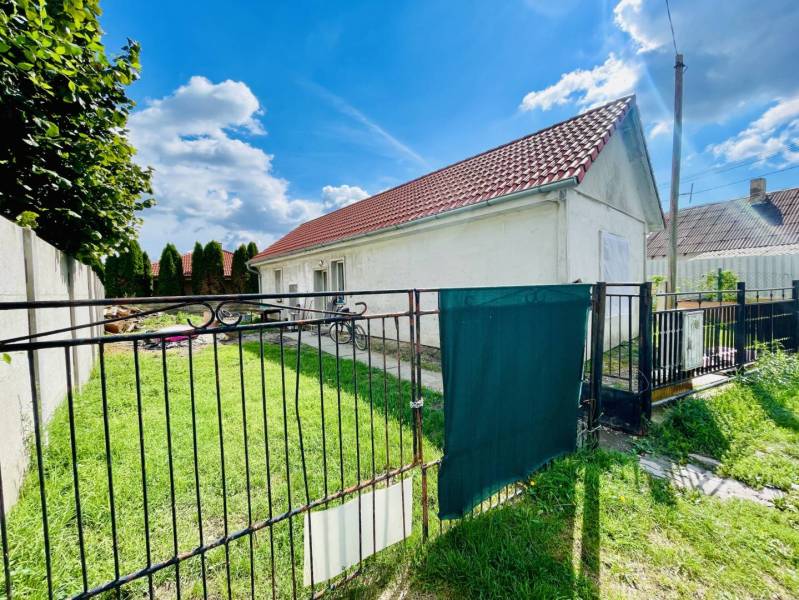 RODINNÝ DOM S ÚTULNÝM POZEMKOM NA PREDAJ V OBCI PATAŠ - Rodinný dom v Pataši s červenou strechou a trávnikom za čiernym plotom.